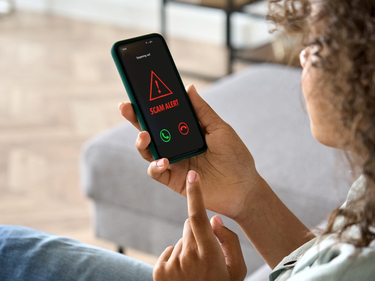 Phone scams Woman holding a smartphone with a scam alert message showing